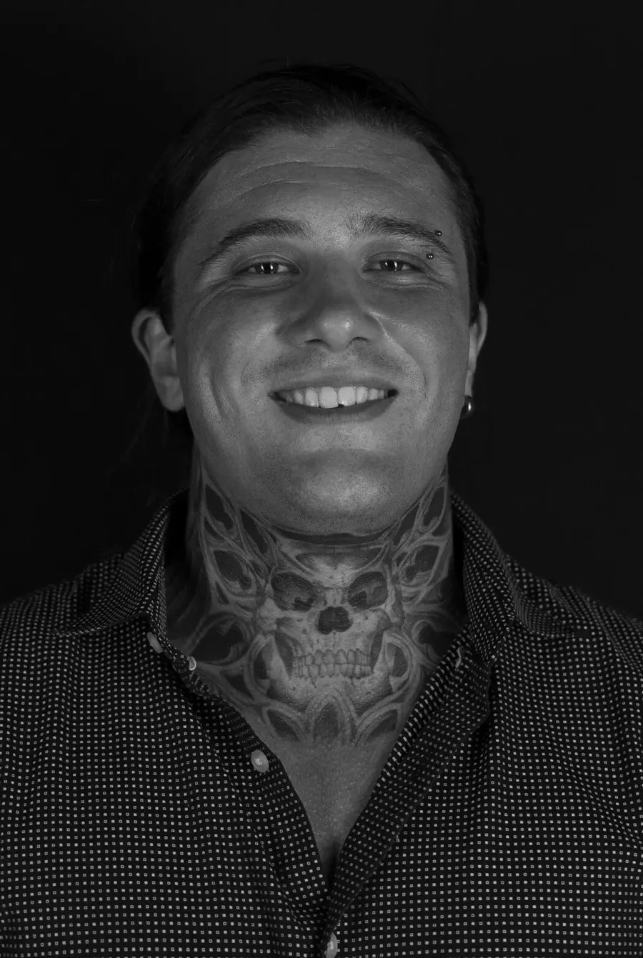 Black-and-white portrait of tattoo artist Clayton Parnell smiling, showing his skull neck tattoo